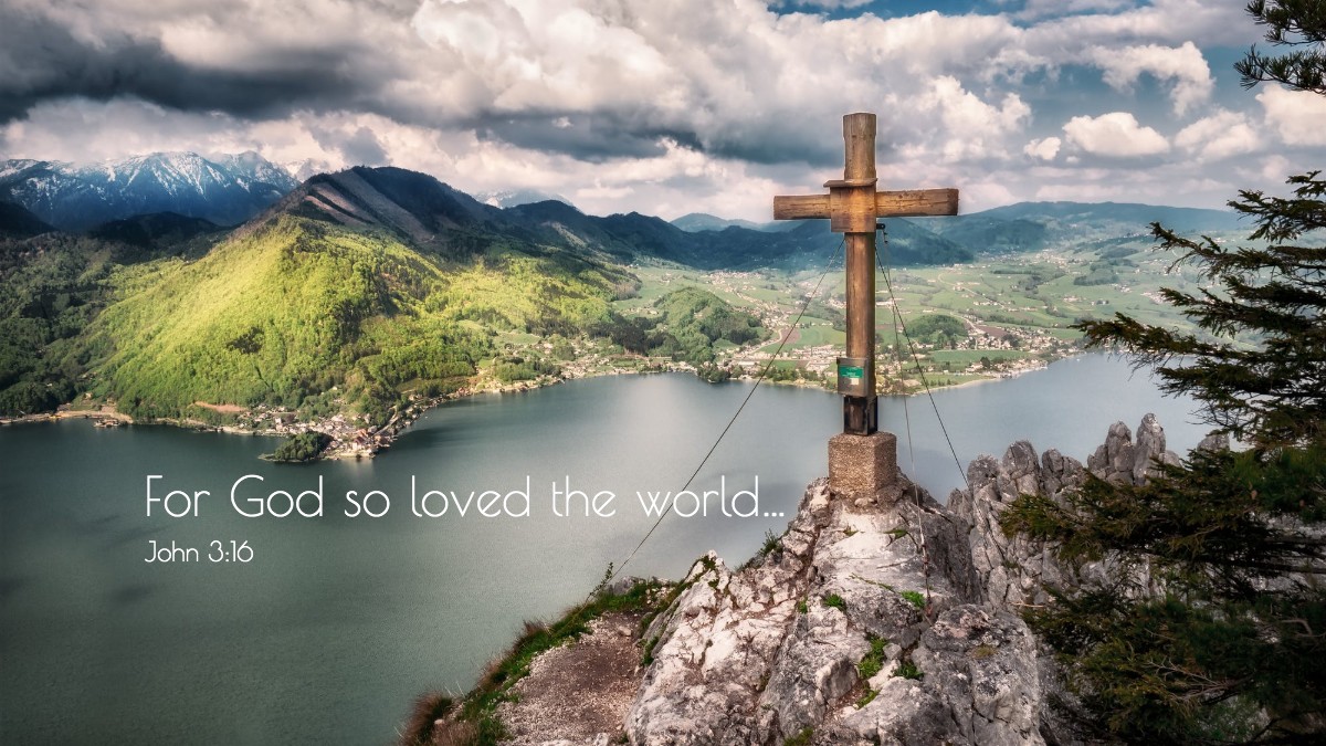 cross on peak in front of lake says, for God so loved the world.