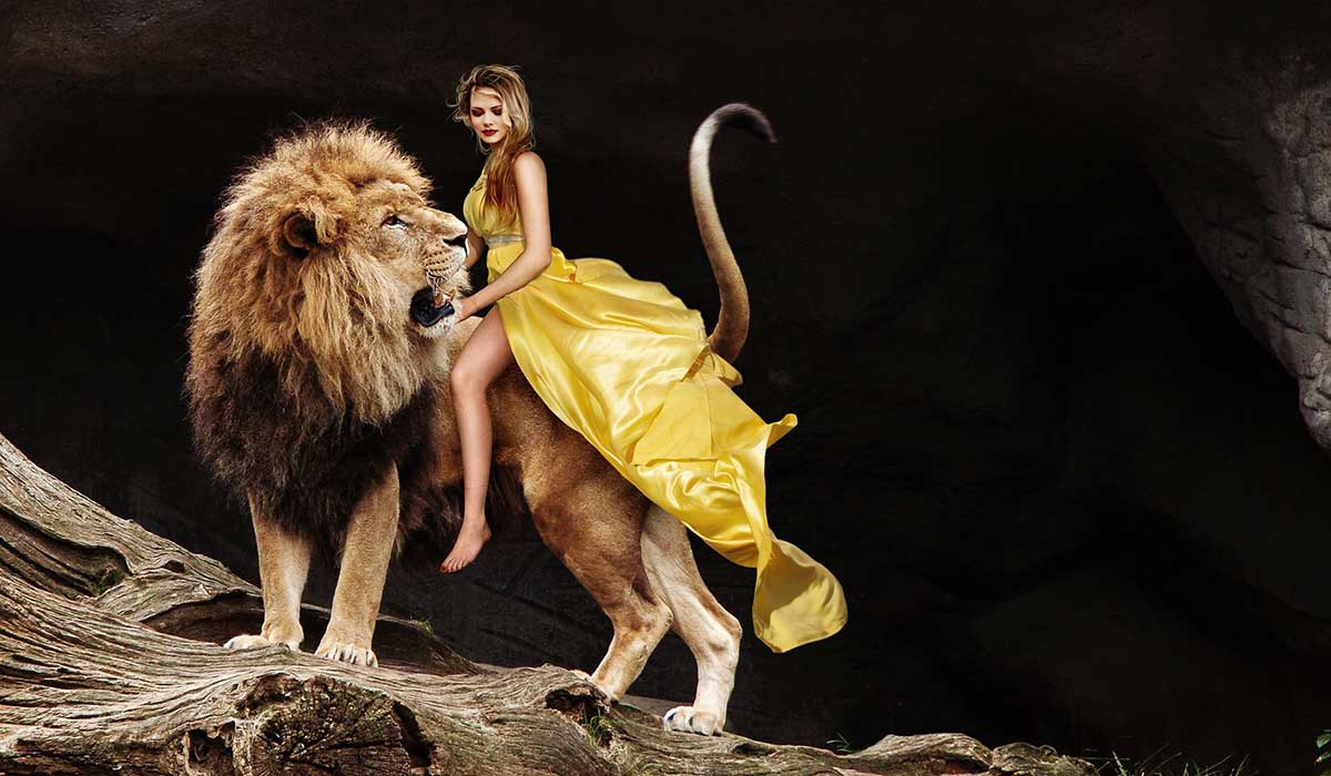 woman in yellow dress riding lion on a cliffside.