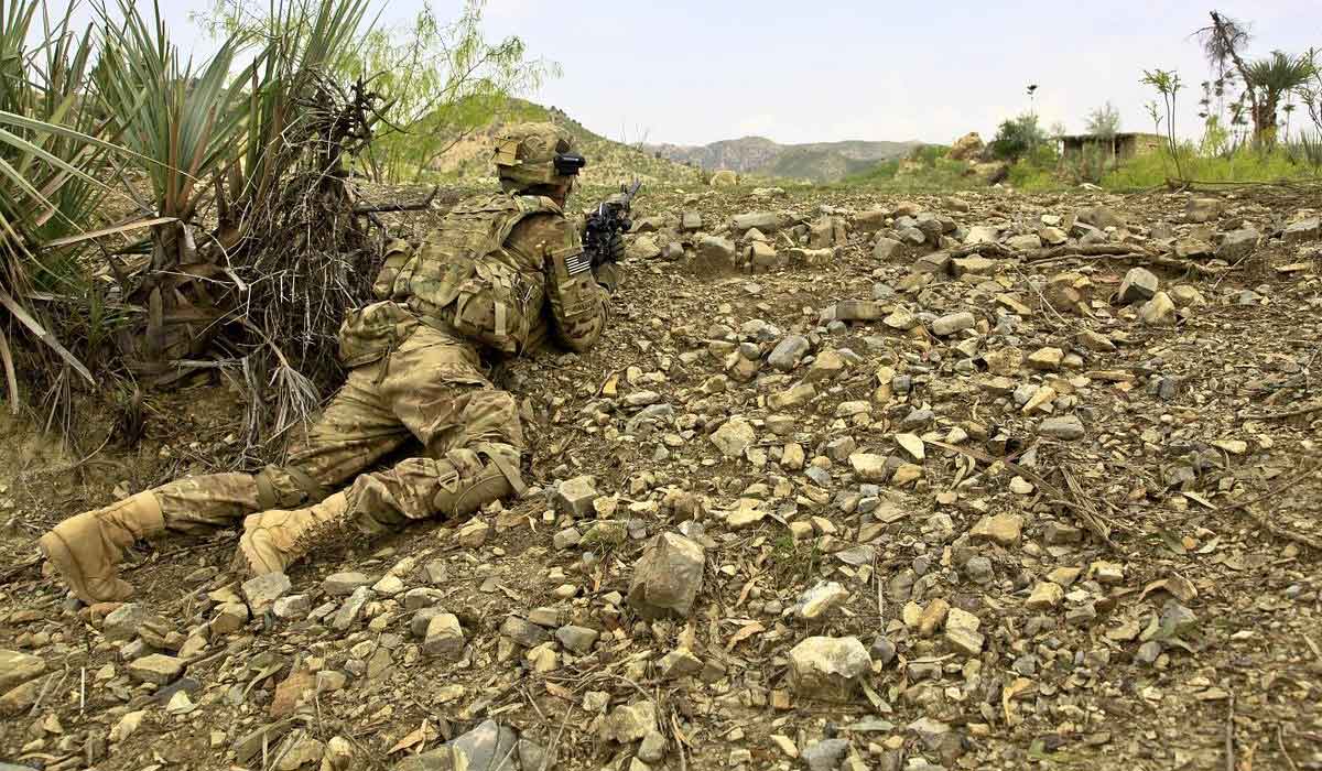 soldier crawling on mossy rocks is camouflaged in his olive green uniform.