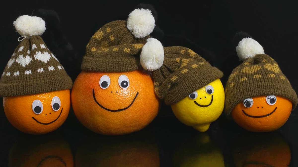 3 oranges and a lemon with smiley faces dressed in brown knit beanies.
