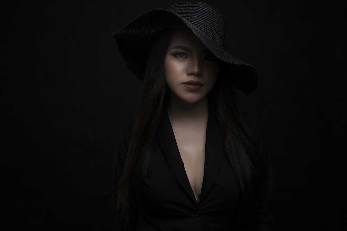 woman shaded by black hat on black background looks mysterious and sophisticated.