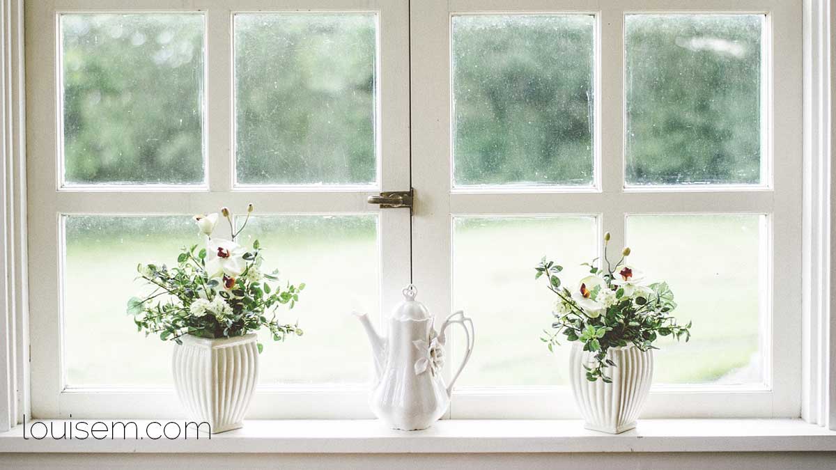 looking outside from in a white room with white roses on the windowsills.